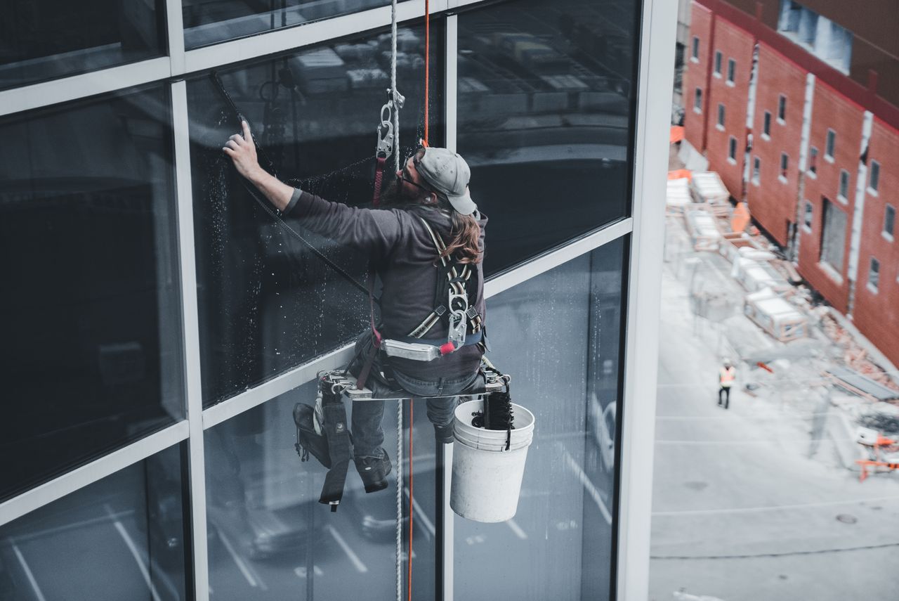 services-01 A worker cleaning skyscraper windows with a harness in an urban setting.