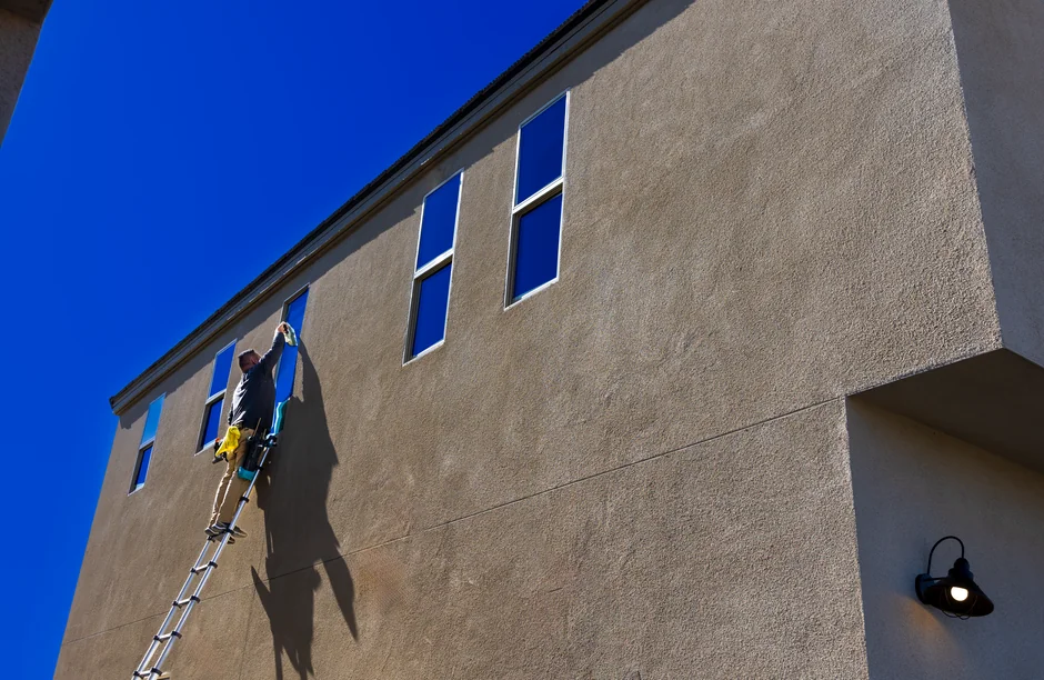 about-01 Deux employés lavent les vitres d’une façade moderne en verre à l’aide d’une plateforme suspendue.